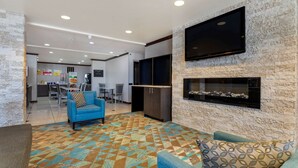 A modern living area with a stone wall, a flat-screen TV, a fireplace, and a patterned carpet. - Quality Inn Sallisaw (Sallisaw)