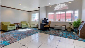 A waiting area with two armchairs, a desk with a computer, a large window, and a patterned floor. - Quality Inn Sallisaw (Sallisaw)