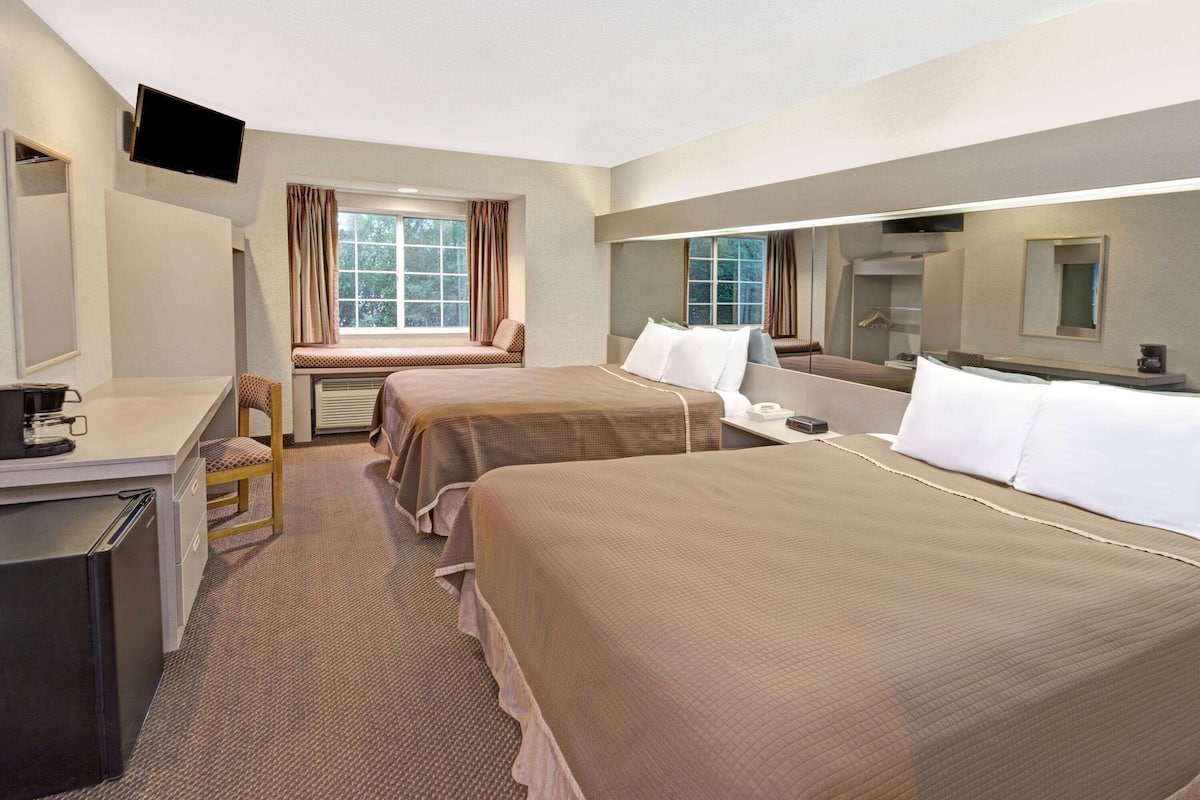 A hotel room with two beds, a desk, a chair, a TV, and a window with curtains.