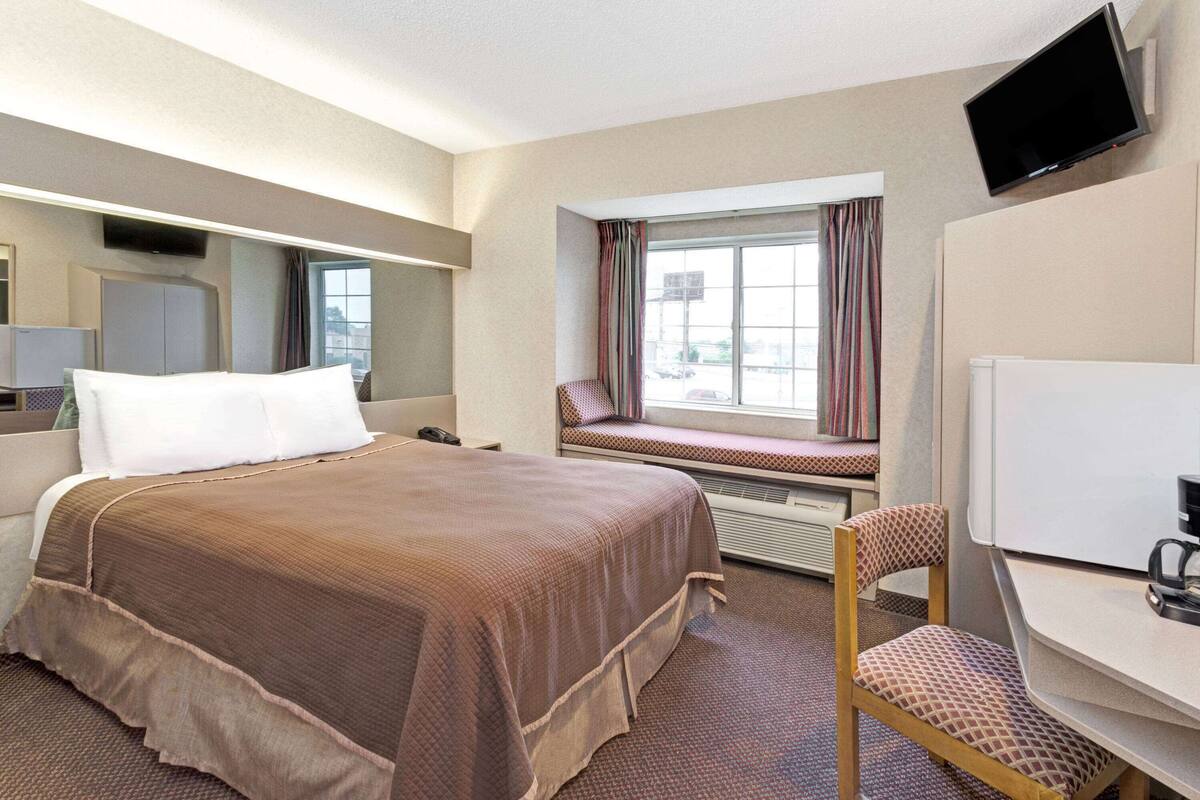 A hotel room with a bed, a desk, a chair, a television, and a window with curtains.
