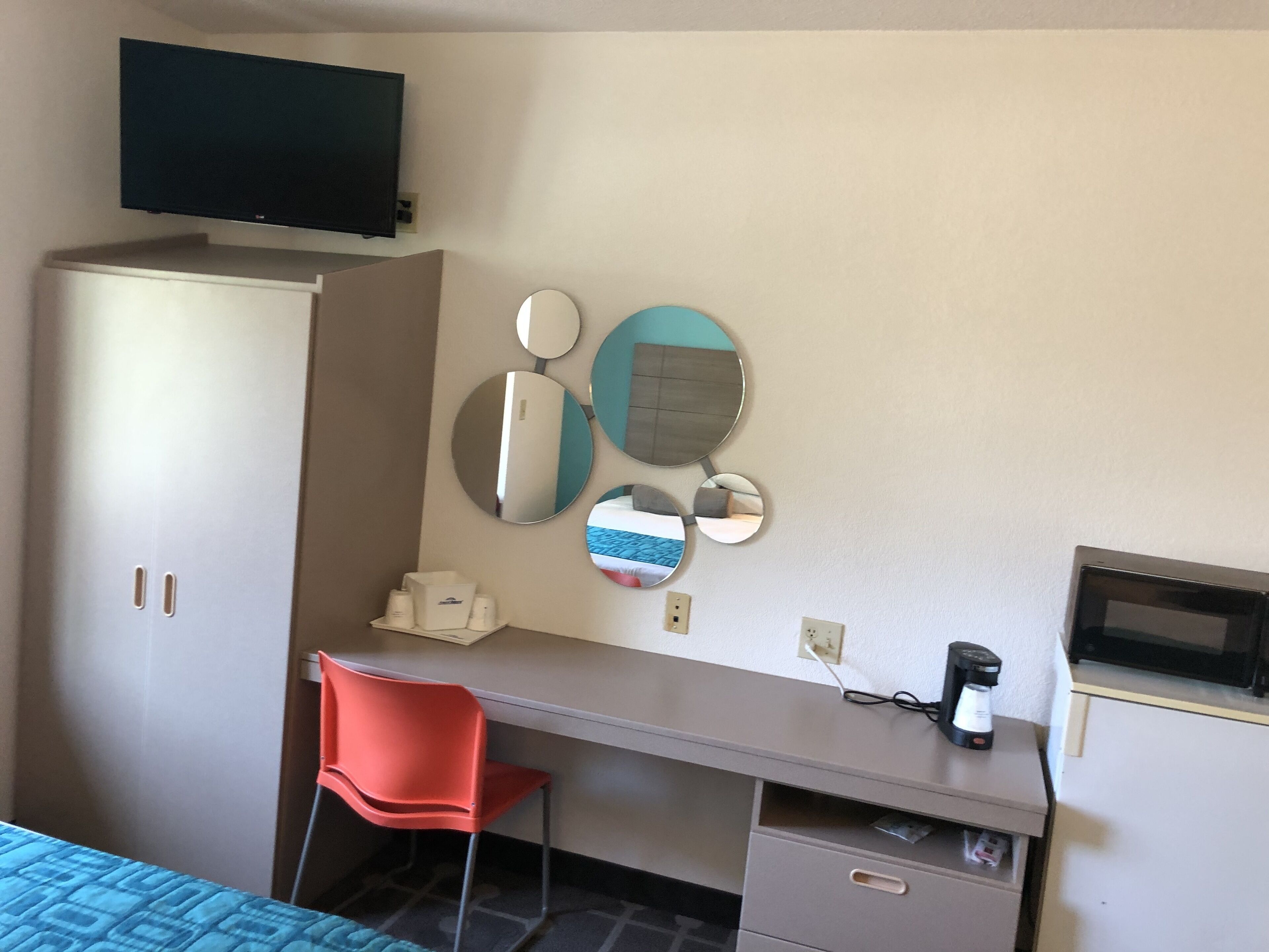 A hotel room with a bed, a desk, a chair, a TV, and a coffee maker.
