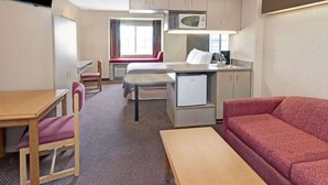 Una habitación de hotel compacta con kitchenette, zona de comedor, sofá y televisión.