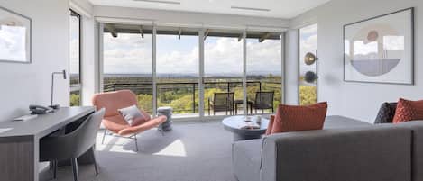 A modern living room with a view of a landscape, a desk with a phone, and a sofa with cushions.