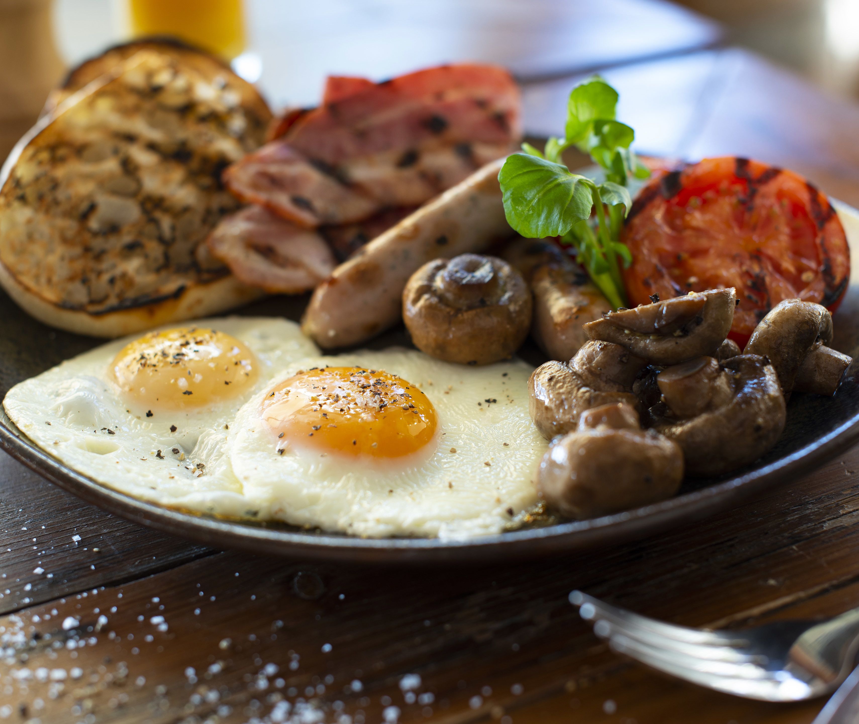 Une assiette de petit-déjeuner comprenant des œufs, des champignons, du bacon et une tomate grillée.