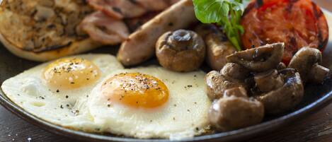 Une assiette de petit-déjeuner comprenant des œufs, des champignons, du bacon et une tomate grillée.