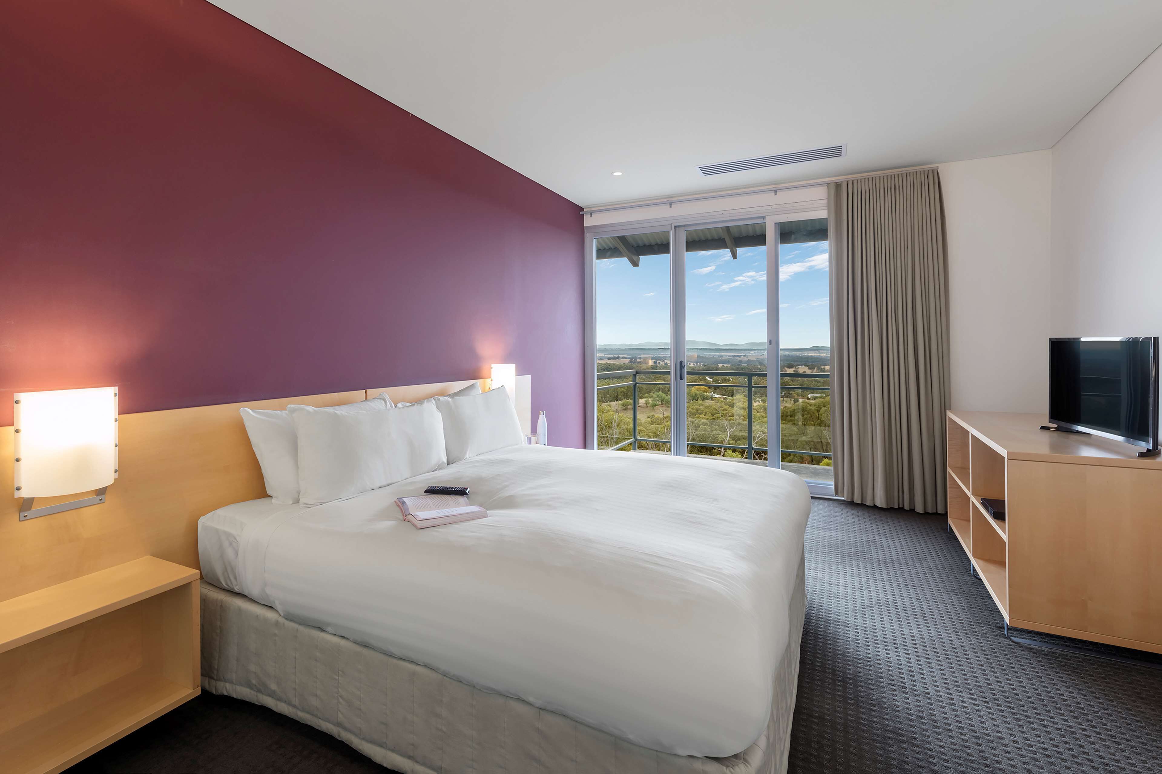 A hotel room with a large bed, a TV, a desk, and a window with a view of the countryside.