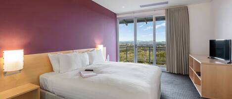A hotel room with a large bed, a TV, a desk, and a window with a view of the countryside.