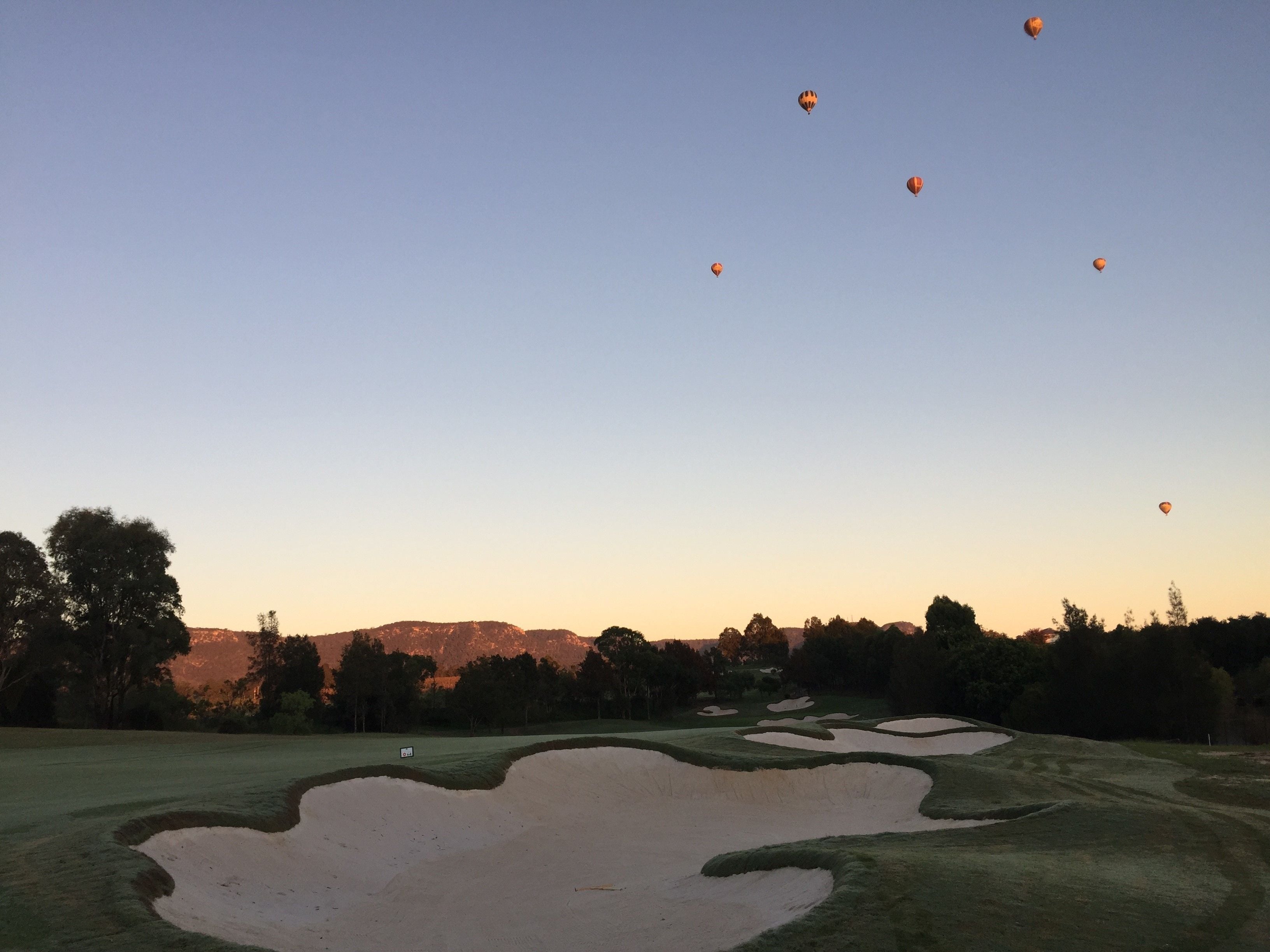 A golf course with sand bunkers and a clear sky.