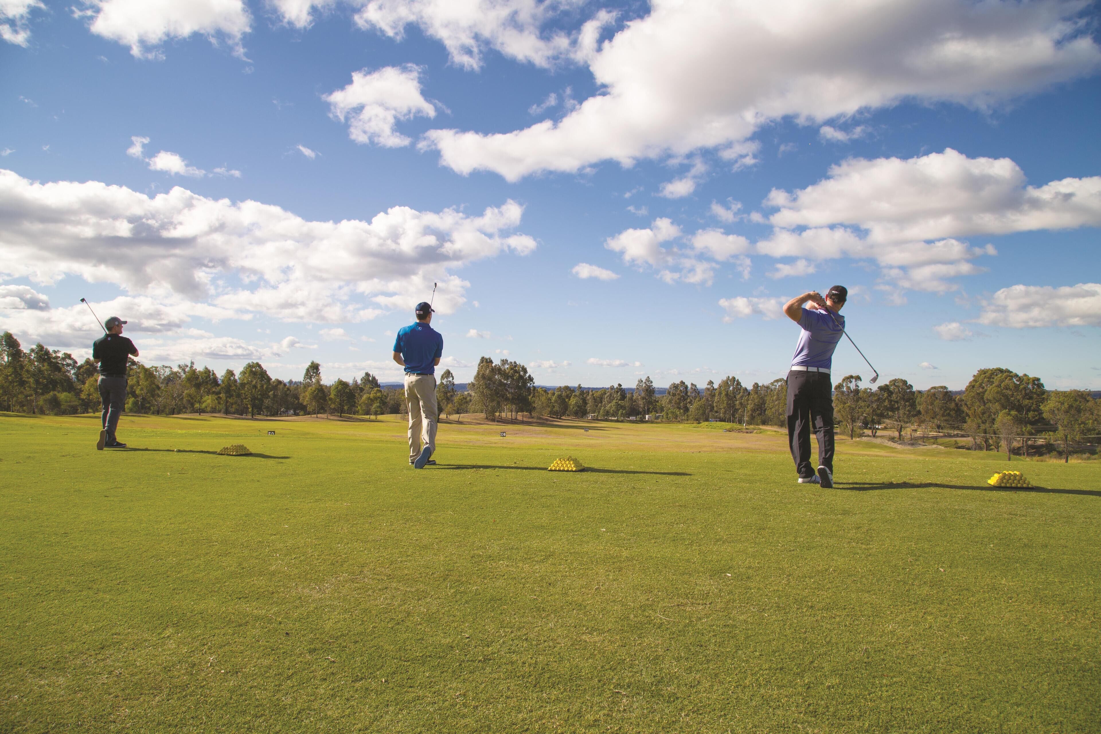 Ein Golfplatz mit drei Spielern in blauen Hemden und schwarzen Hosen.