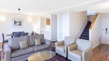 Un salon moderne avec un canapé, des fauteuils, une table basse en verre et un escalier.