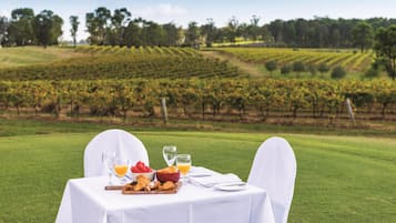 Une table dressée à l’extérieur, avec vue sur un vignoble, un saladier rempli de fruits et un croissant.
