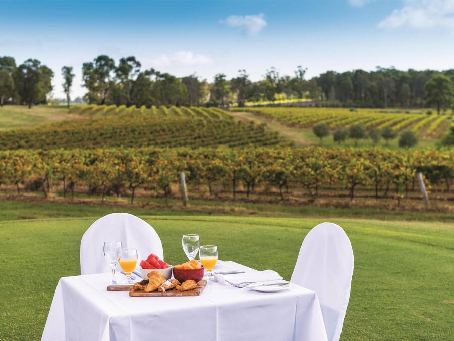 Une table dressée à l’extérieur, avec vue sur un vignoble, un saladier rempli de fruits et un croissant.