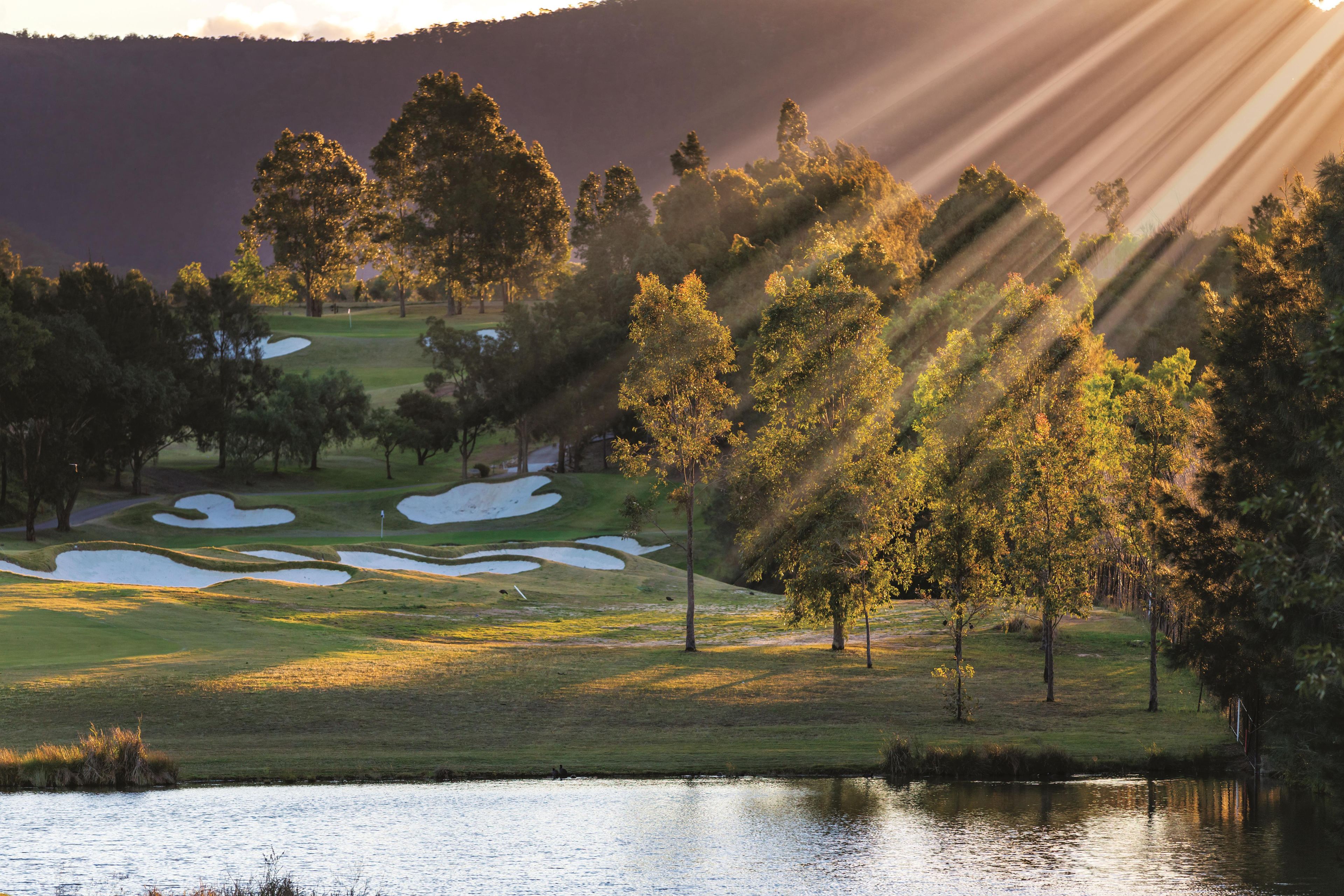 Un campo de golf con búnkeres de arena, árboles y una masa de agua.