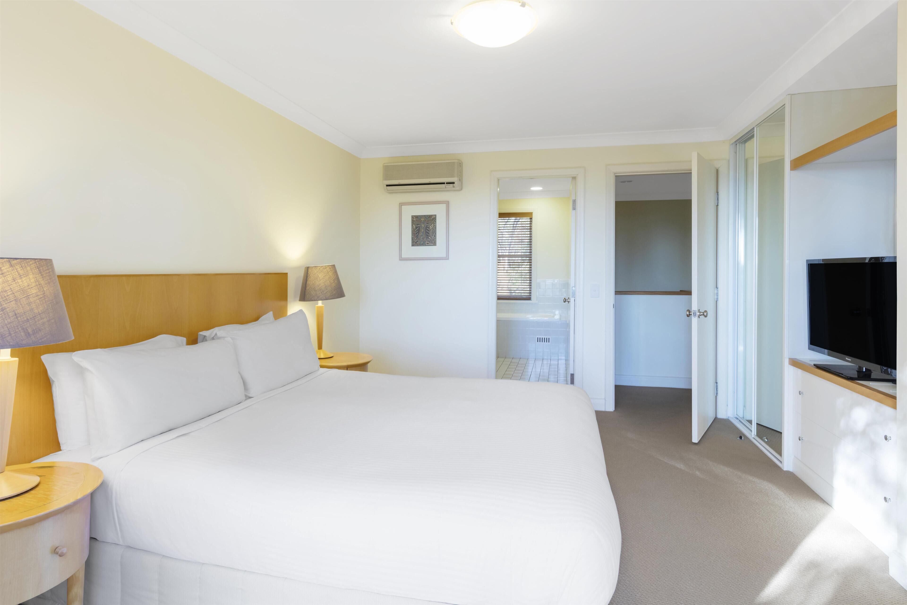 A hotel room with a large bed, bedside lamps, a flat-screen TV, and a wardrobe.