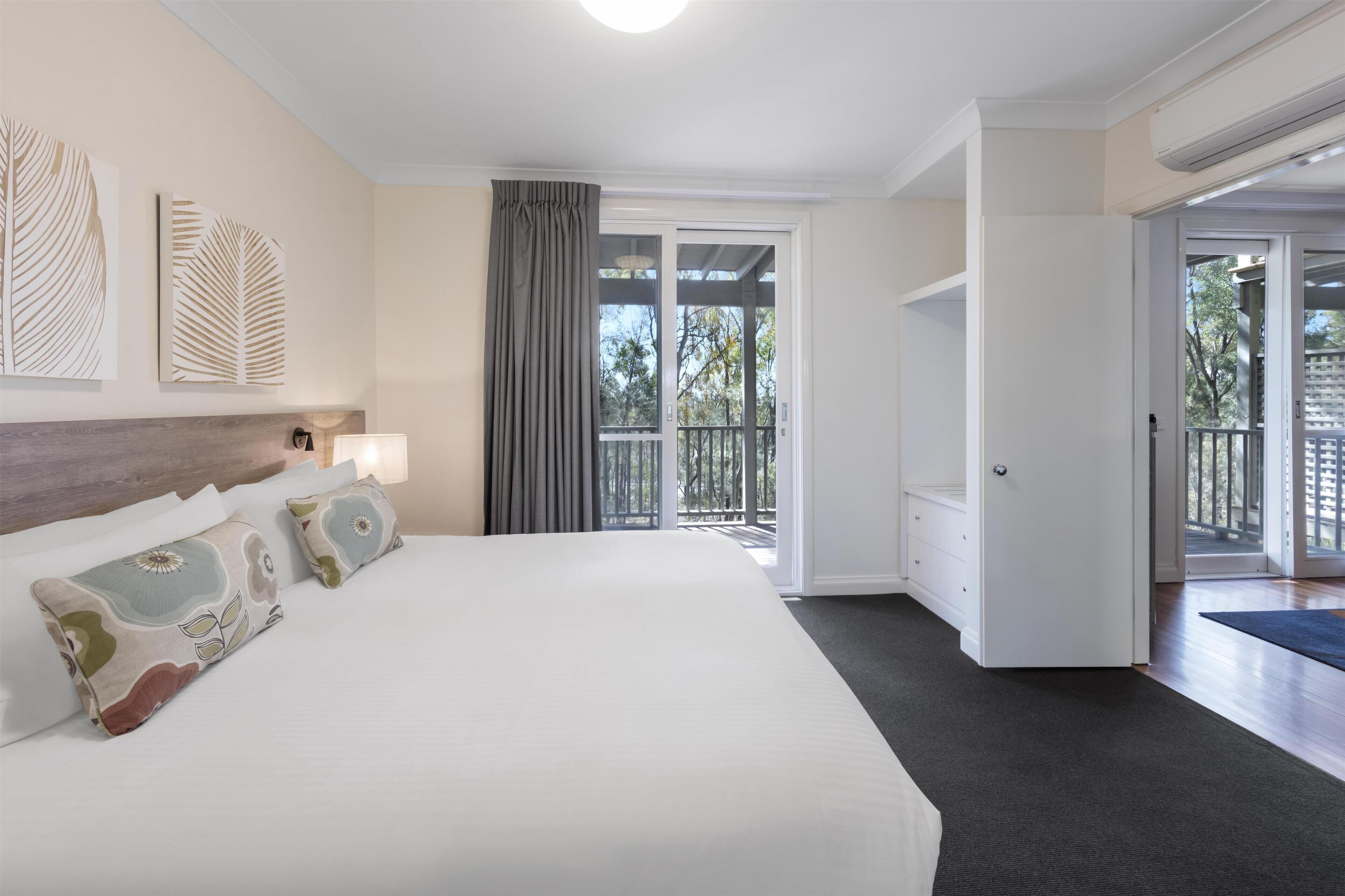 A hotel room with a large bed, a nightstand with a lamp, a view of the outdoors through a sliding door, and a balcony.