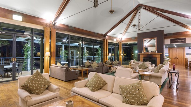 A spacious lounge area with multiple sofas and armchairs, wooden flooring, and large windows offering views of the outdoors. - Oaks Cypress Lakes Resort (Pokolbin)