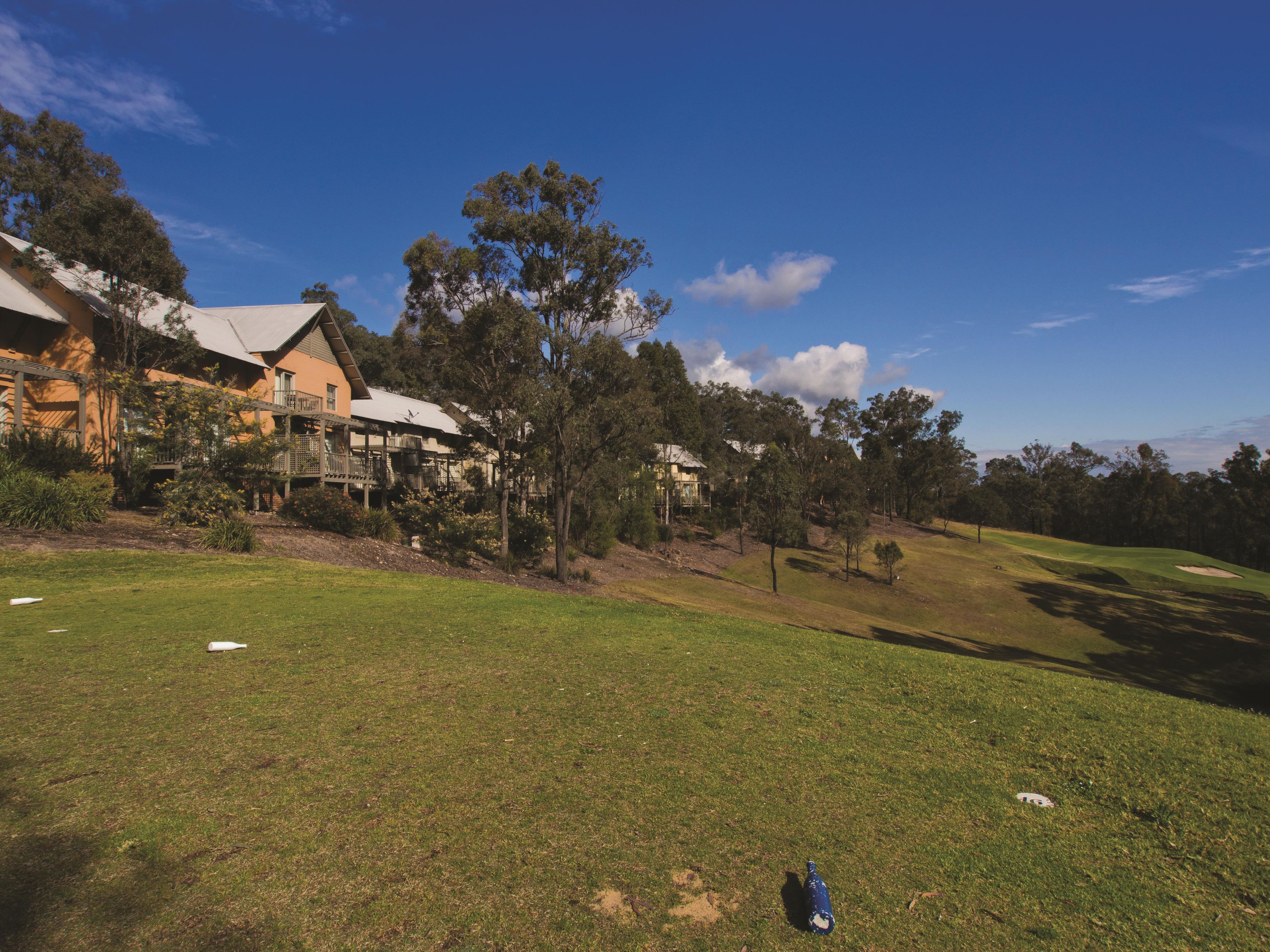 A golf course with a clubhouse, trees, and a clear sky.