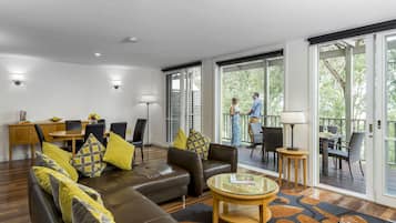 A modern living room with a brown leather sofa, yellow and gray patterned pillows, a round coffee table, and a dining area with a wooden table and chairs.