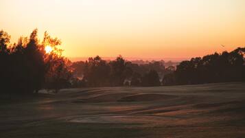 Un terrain de golf au coucher du soleil, avec des arbres et un ciel dégagé.