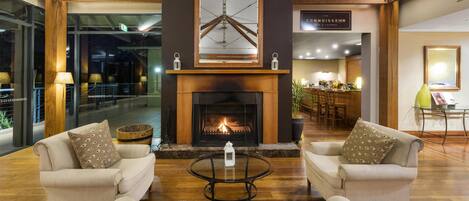 A cozy lobby with two sofas facing a fireplace, a coffee table, and a large mirror above the fireplace.