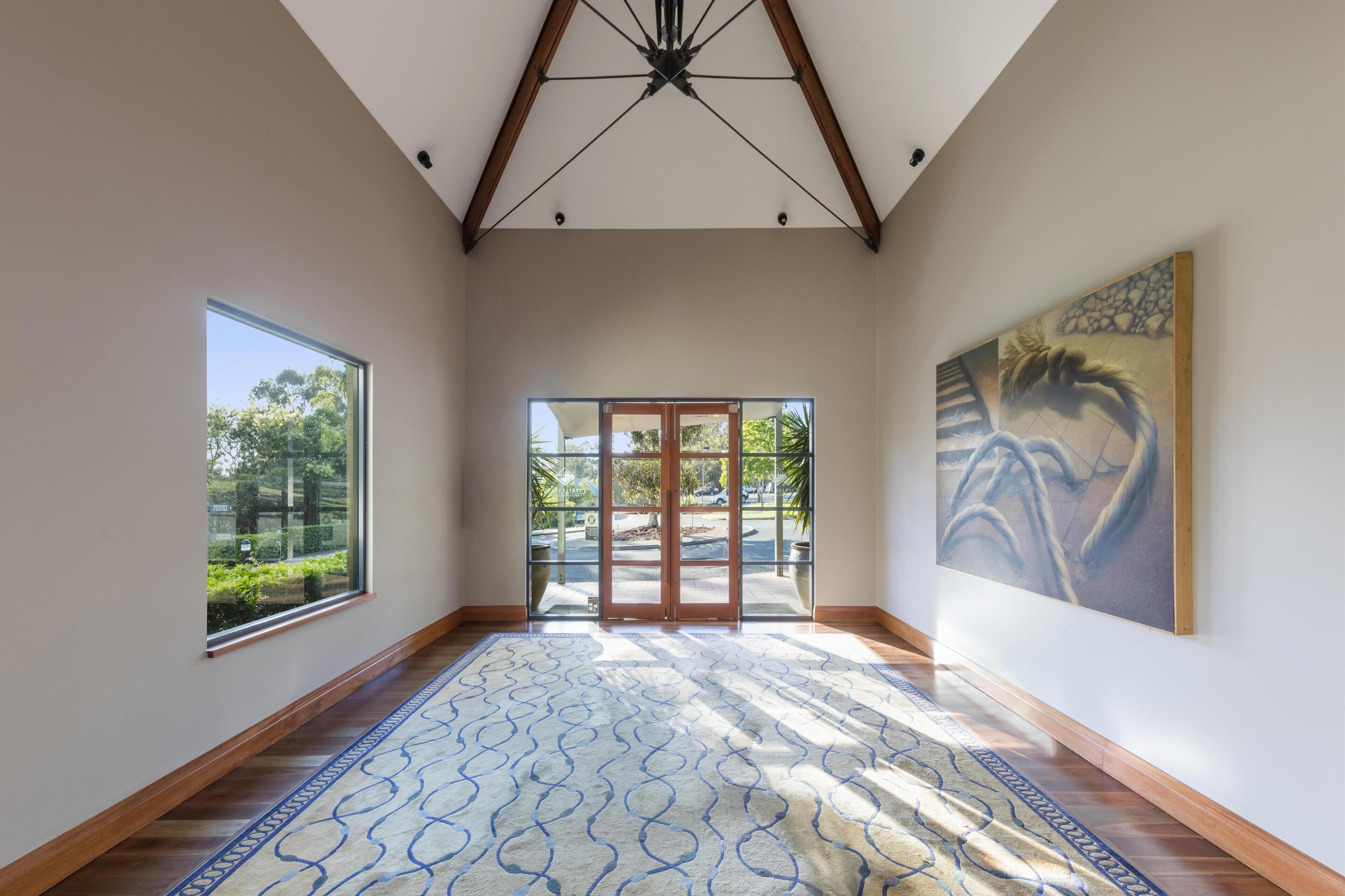 Una habitación amplia con techo alto, ventanas grandes y una alfombra estampada.