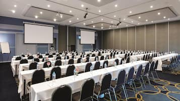 Une salle de conférence avec des rangées de tables, des chaises et un grand écran.