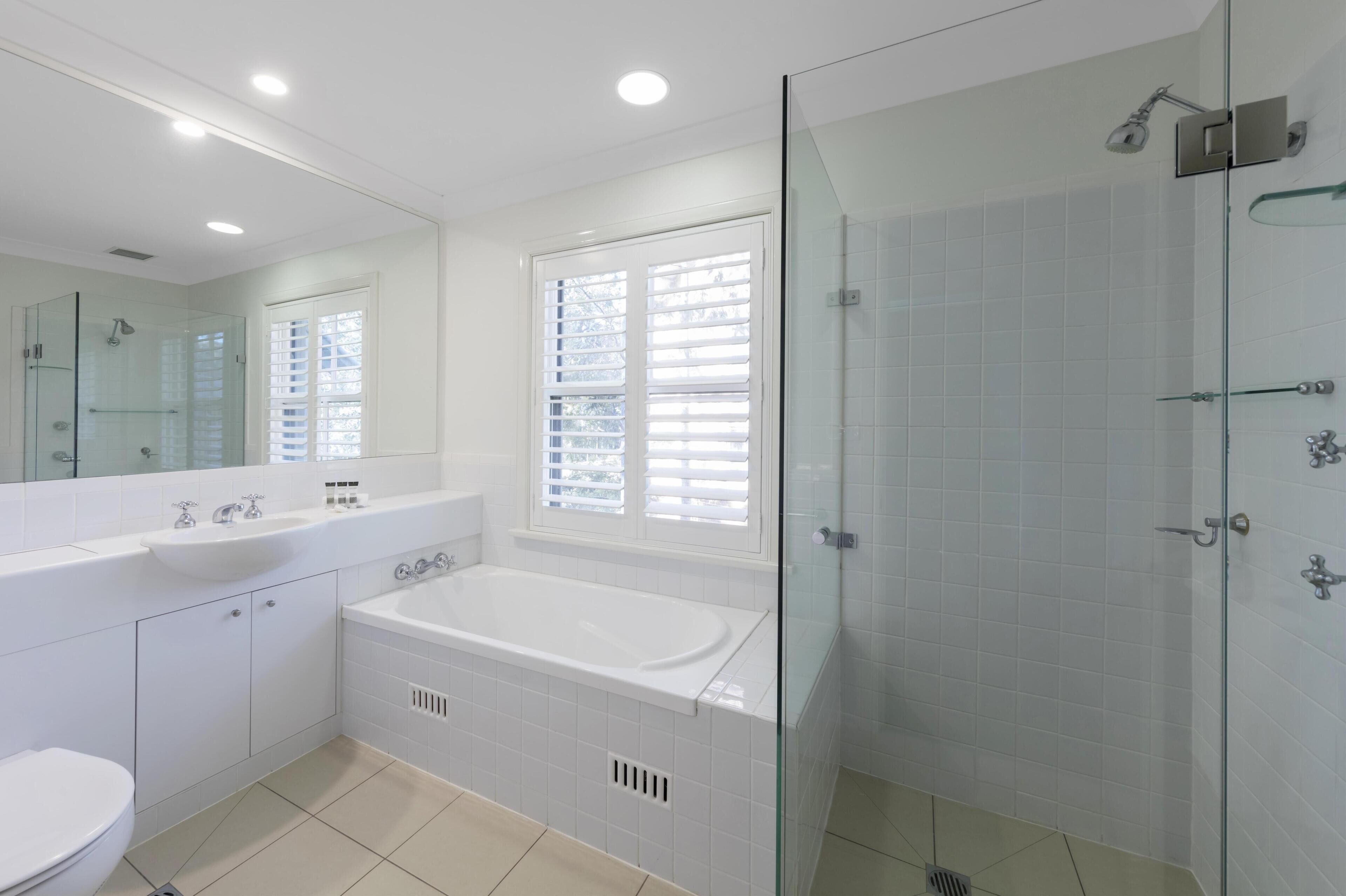 A modern bathroom with a glass-enclosed shower, a large bathtub, and a vanity with a sink and mirror.
