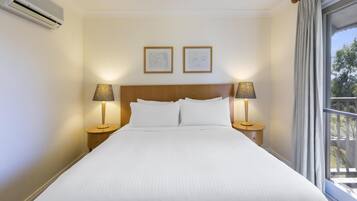 Una camera d'albergo con un letto grande, due lampade ai comodini, un condizionatore d'aria e due opere d'arte incorniciate appese al muro.