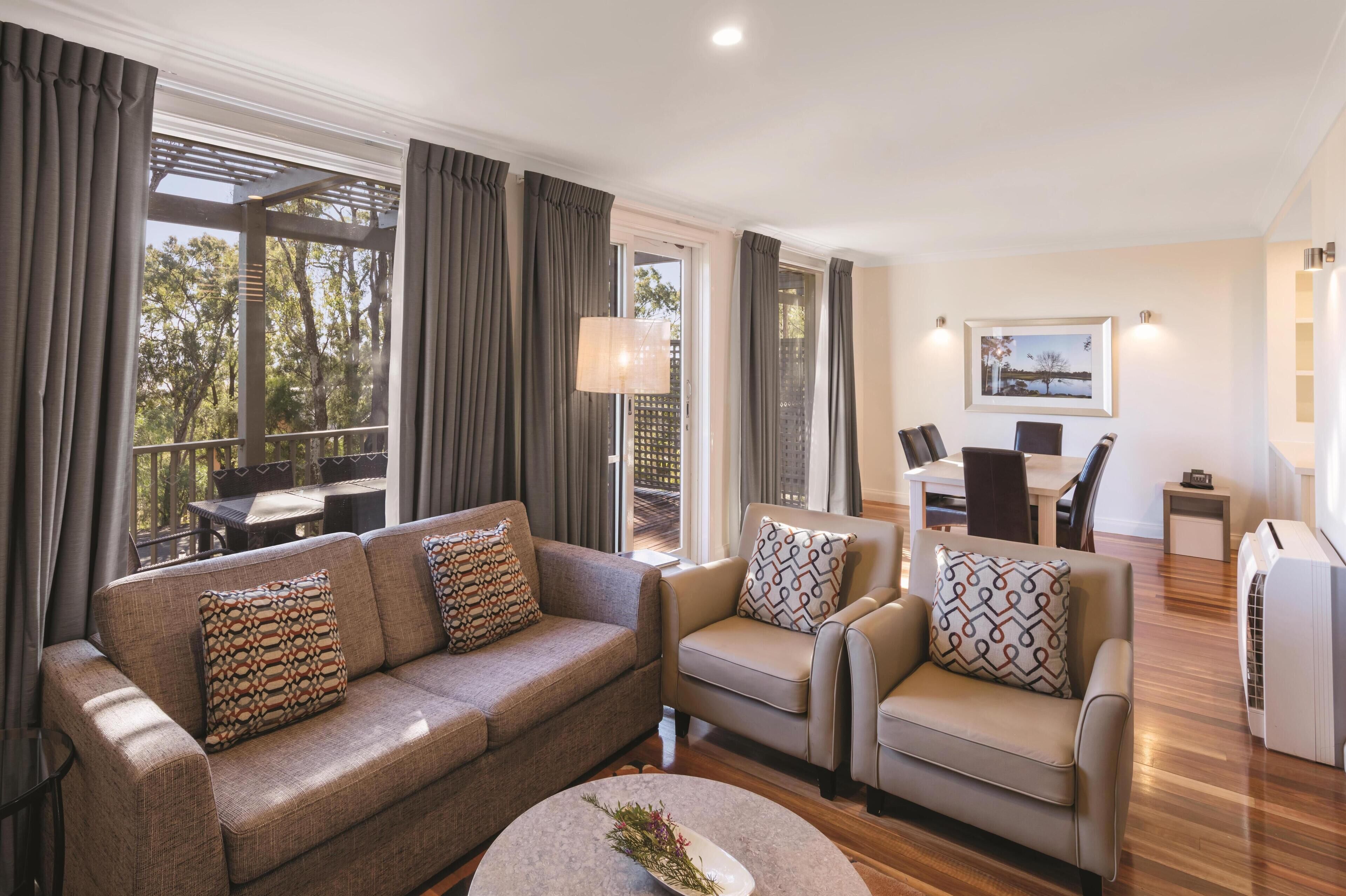 A modern living room with a sofa, two armchairs, a coffee table, and a dining area with a table and chairs.