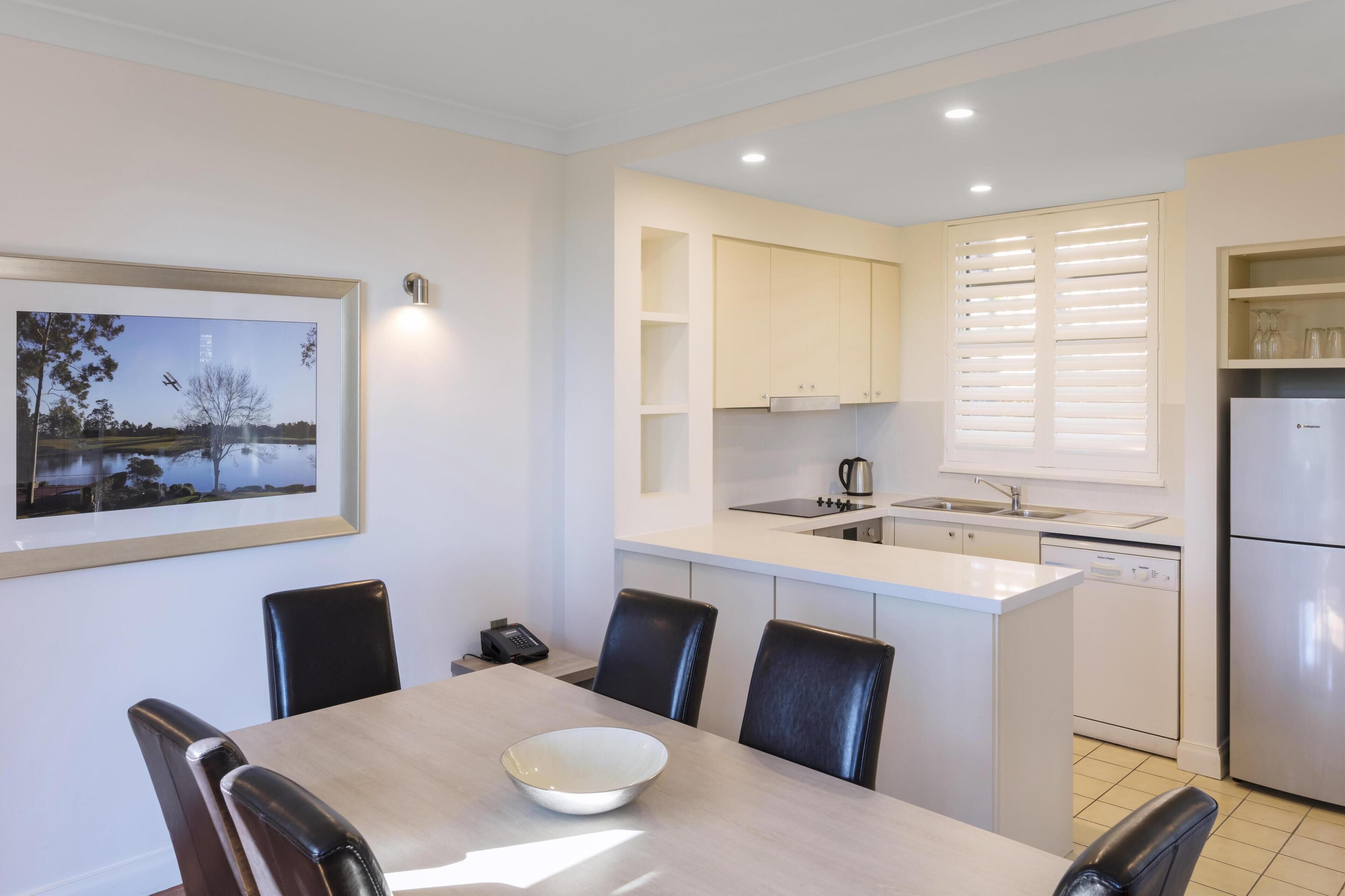 A modern kitchen with white cabinetry, a built-in island, and a dining area with a table and chairs.
