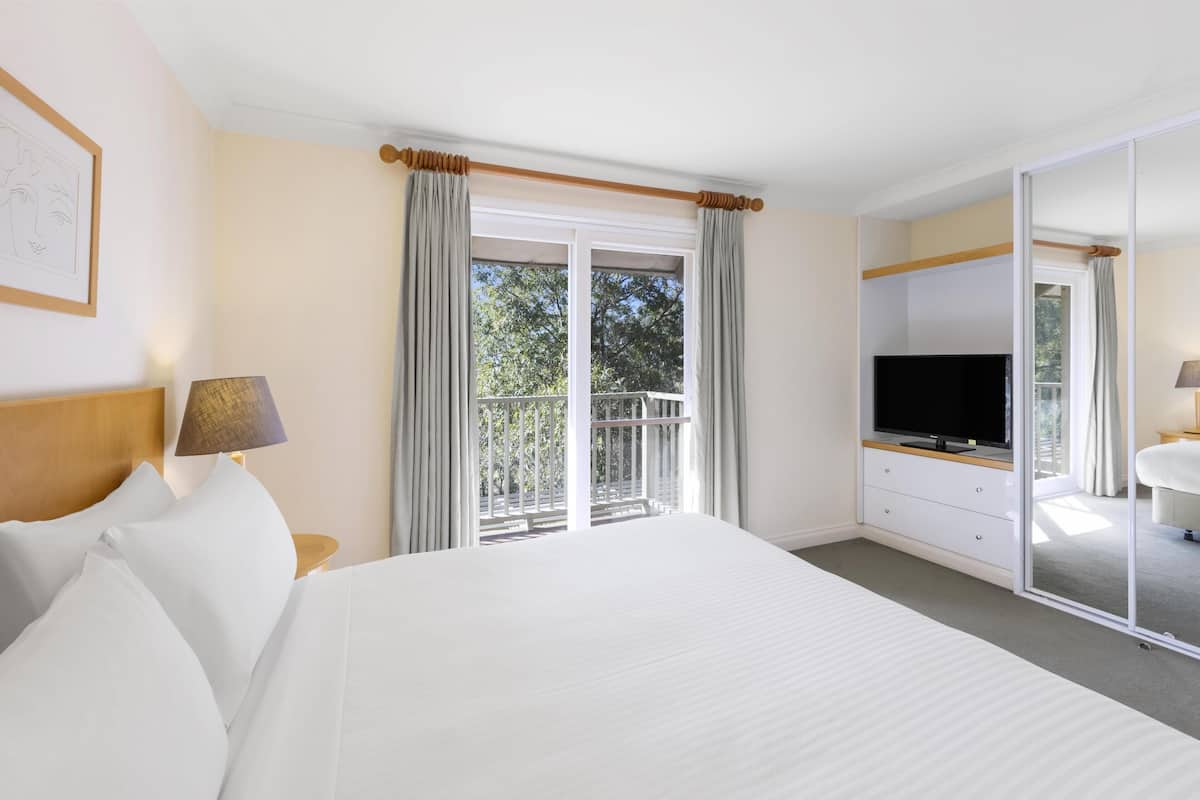 Une chambre d’hôtel avec un grand lit, une télévision, un bureau avec une lampe et une porte-fenêtre coulissante donnant sur un balcon.