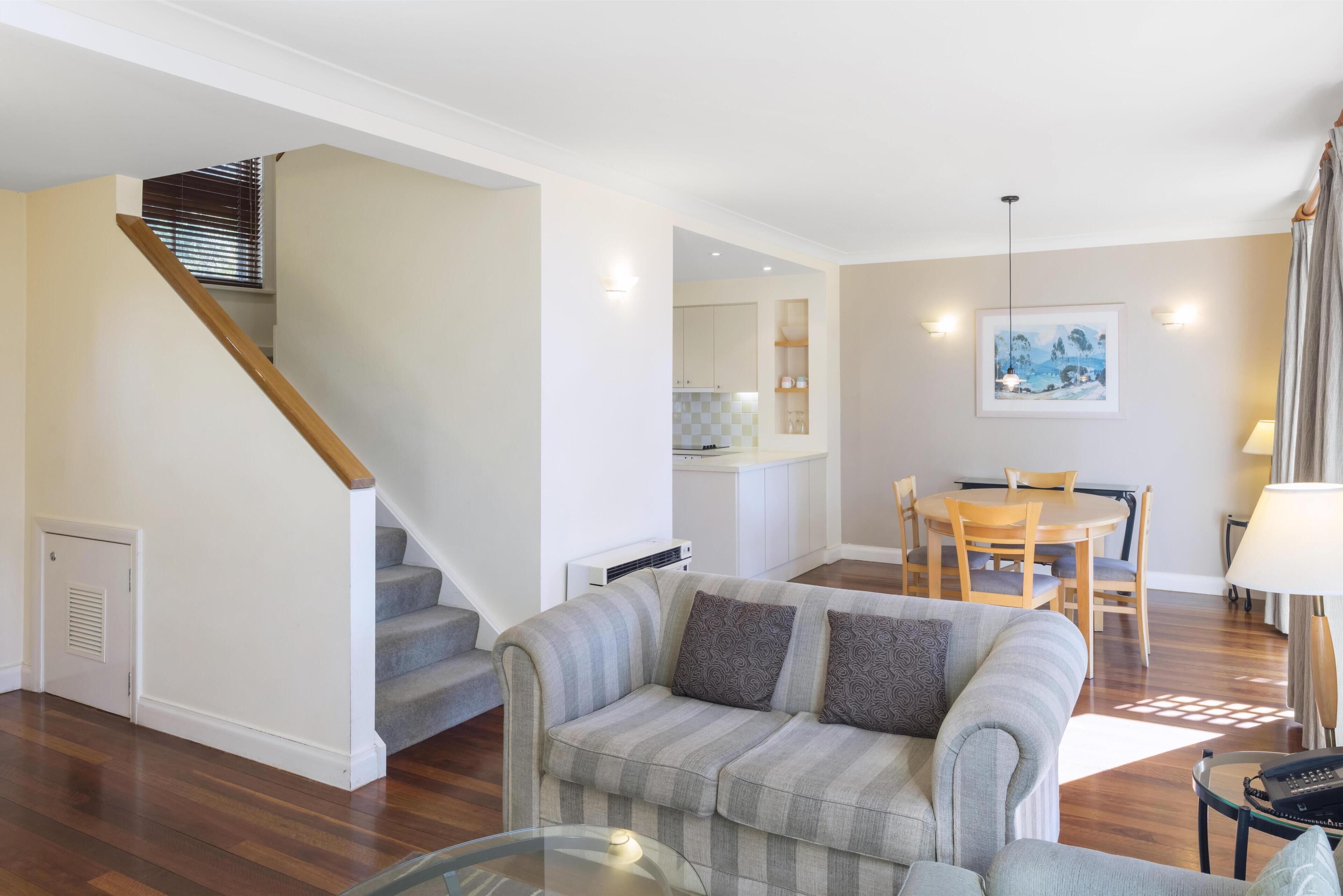 A modern living room with a staircase, a dining area, and a kitchen in the background.