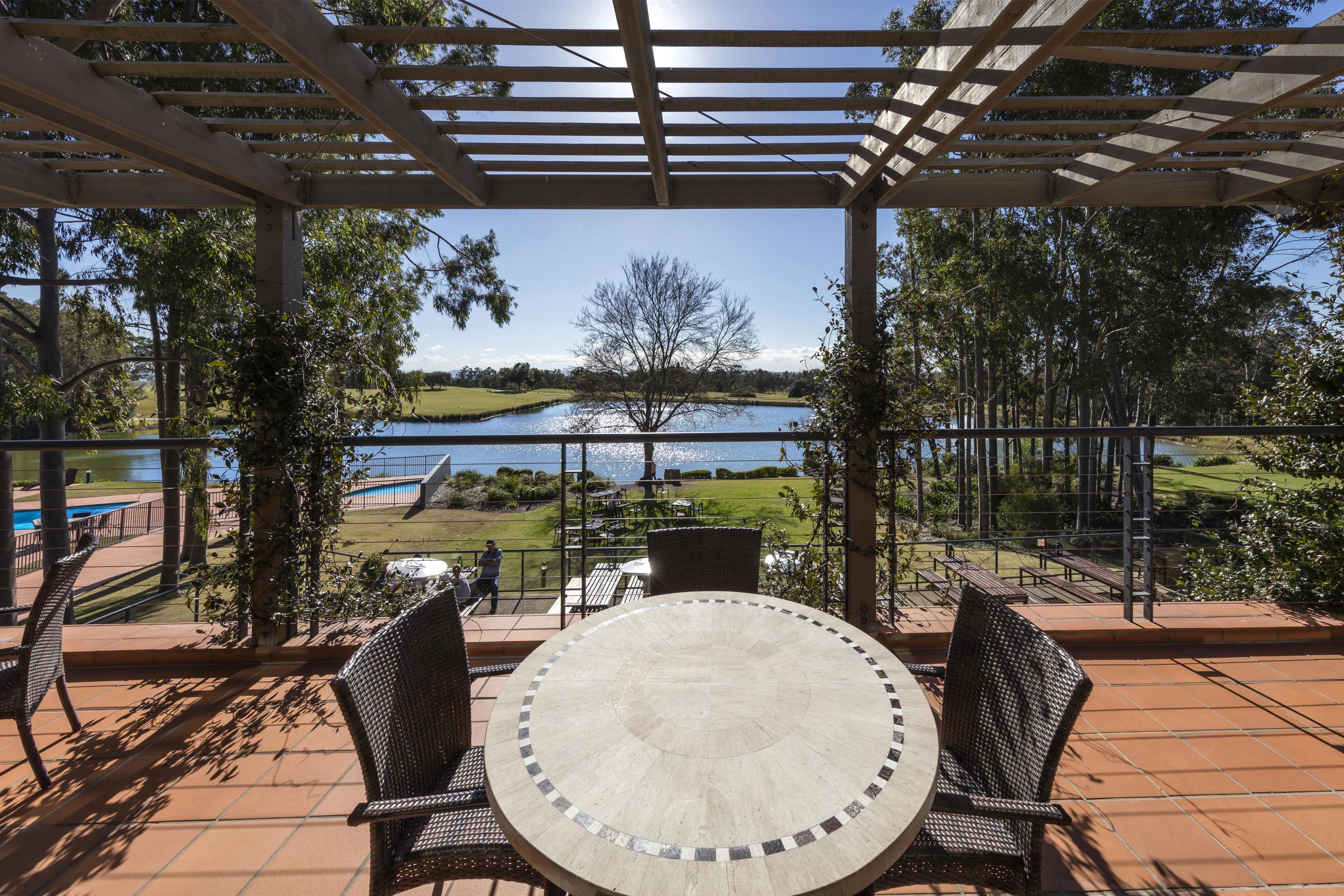 A covered patio with a round table and chairs, overlooking a lake and golf course.