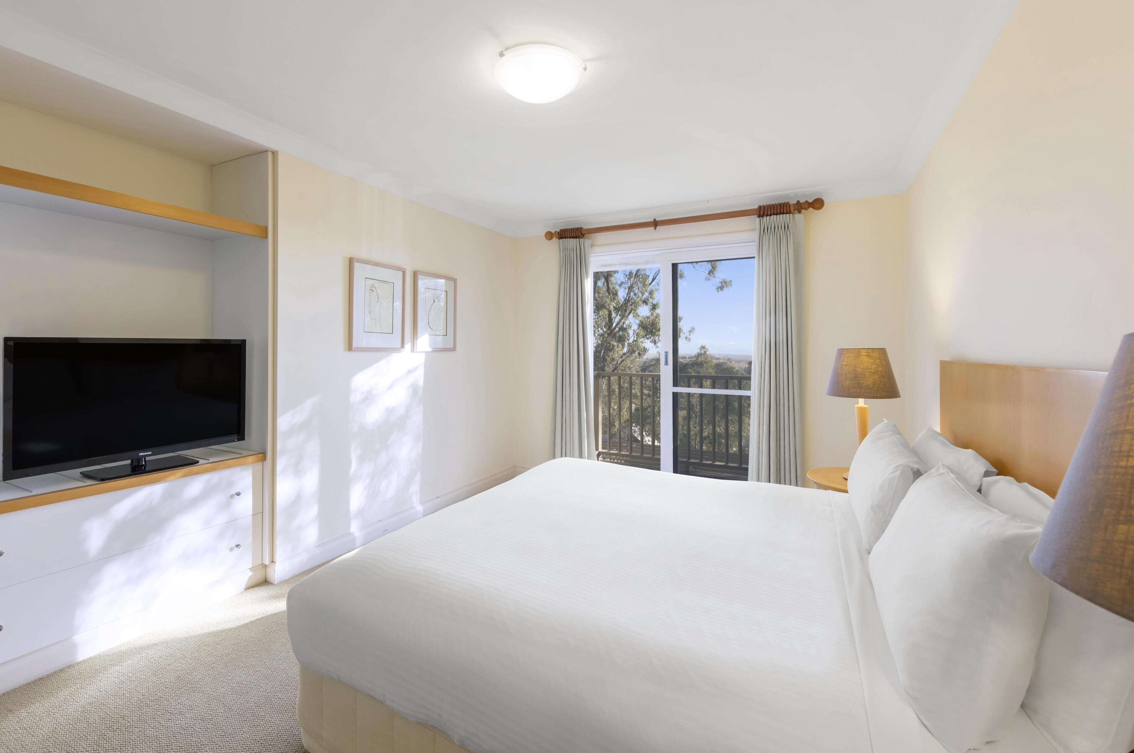 A hotel room with a bed, a TV, a window with curtains, and a lamp.