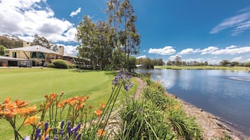 A golf course with a clubhouse, a body of water, and a variety of flowers in the foreground.