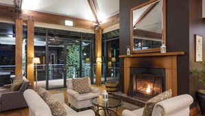 A modern living room with a fireplace, comfortable seating, and large windows offering a view of the outdoors. - Oaks Cypress Lakes Resort (Pokolbin)