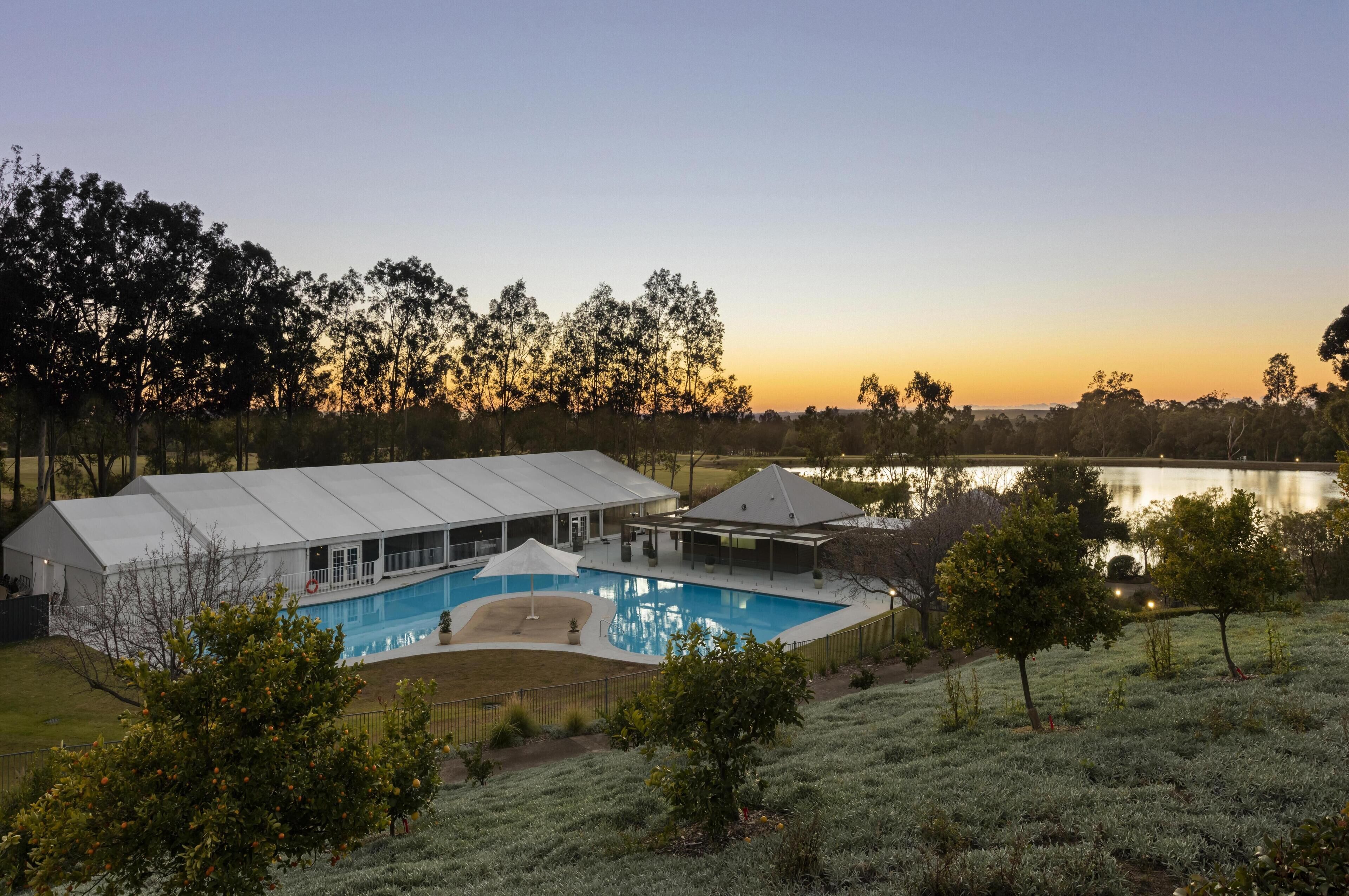 A house with a swimming pool, a covered patio, and a view of a lake at sunset.