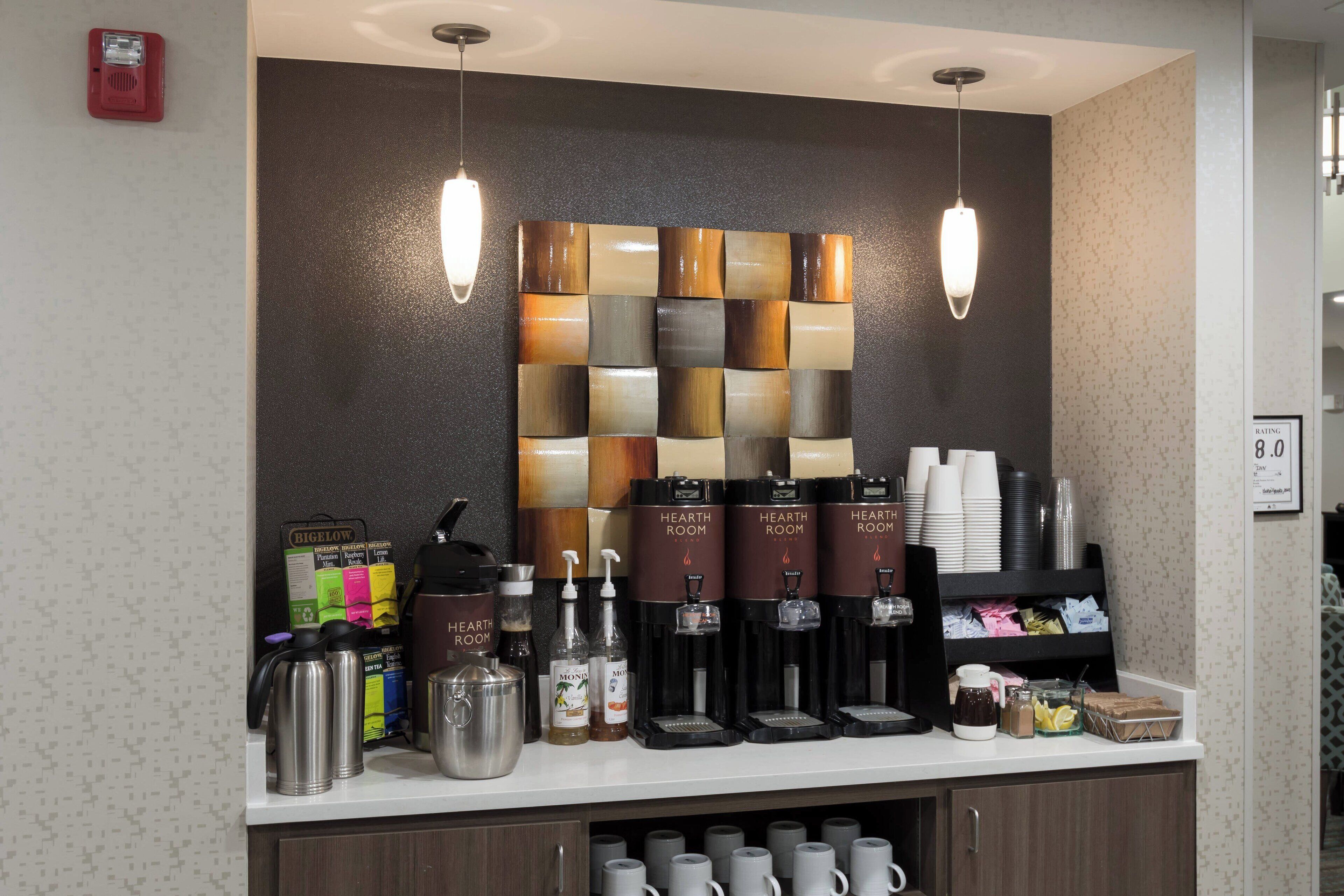 Uma estação de café com vários dispensadores, uma seleção de canecas e variedade de cápsulas de café.