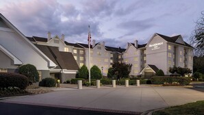 Hotel com design moderno, apresentando um mastro central, um gramado bem cuidado e um céu claro.