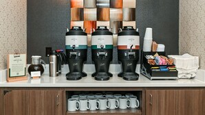 Um espaço para café com três máquinas de café, um jarro e uma pilha de copos descartáveis.