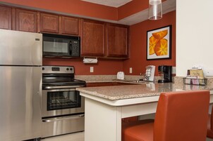 Una cocina con electrodomésticos de acero inoxidable, armarios de madera, encimera de granito y una silla roja.
