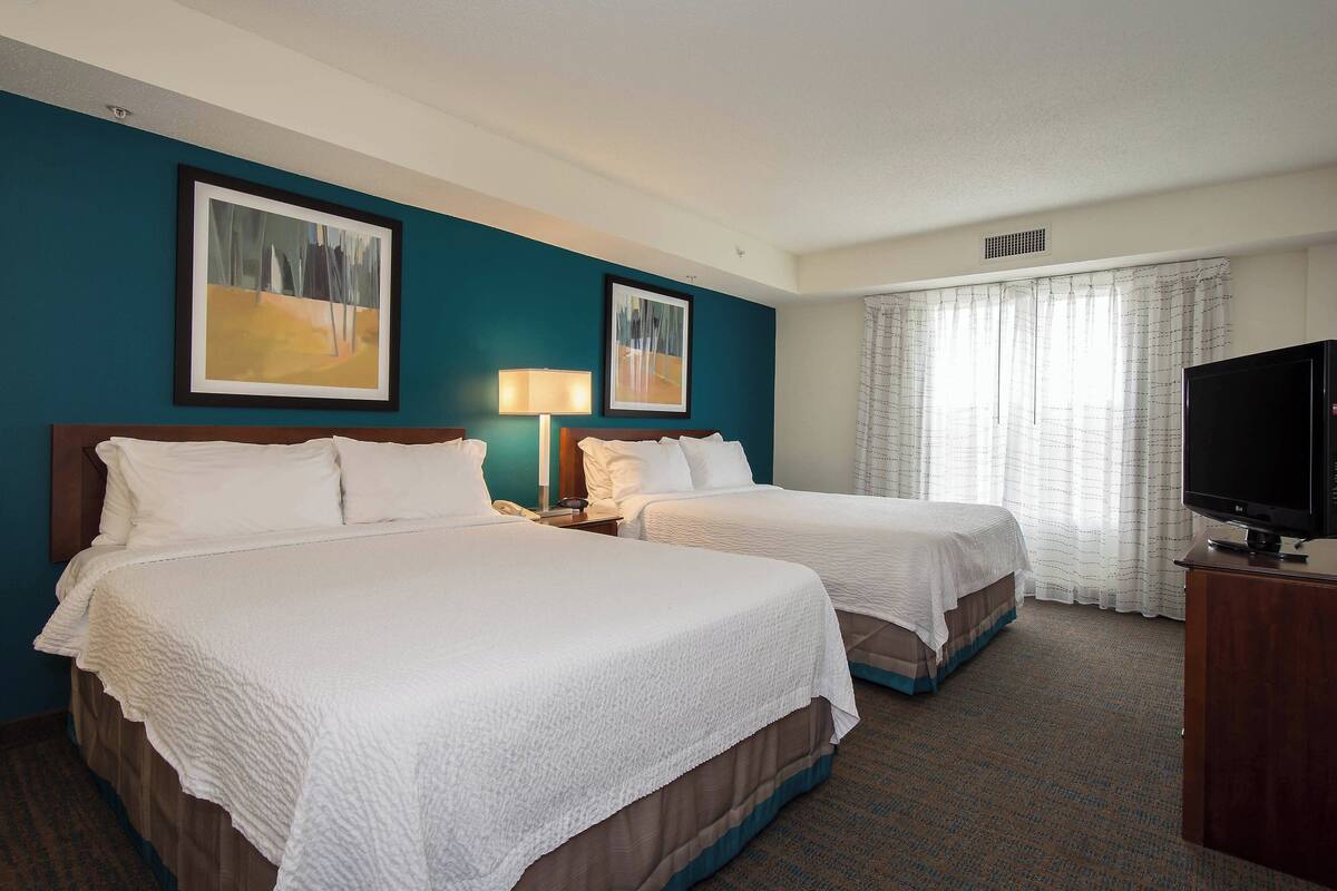A hotel room with two beds, a television on a stand, and artwork on the walls.
