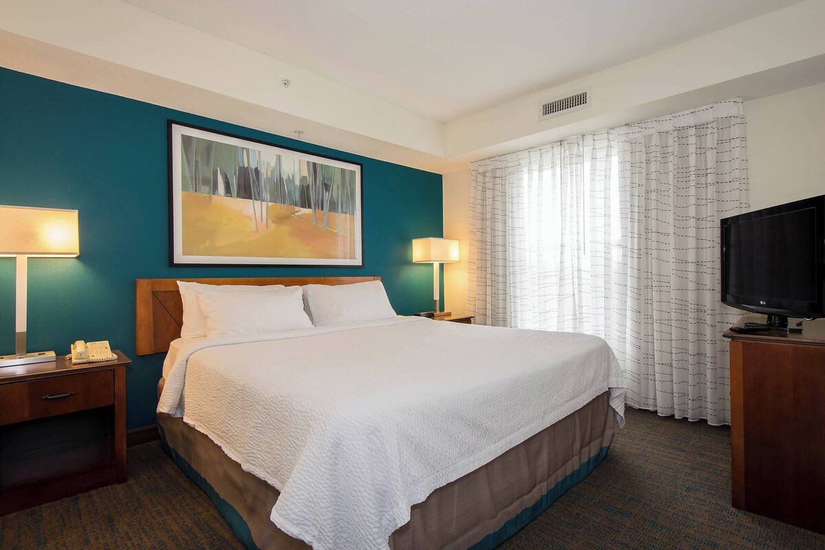 A hotel room with a large bed, two bedside tables with lamps, a flat-screen TV, and a painting on the wall.