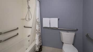 Un baño con bañera, inodoro y barras de apoyo.