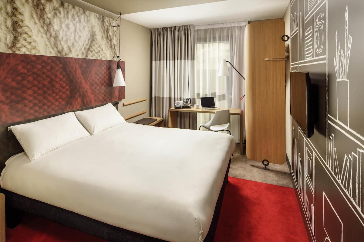 A hotel room with a bed, desk, chair, and a TV on the wall.