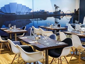 Een restaurant met gedekte tafels, stoelen en uitzicht op de stad.