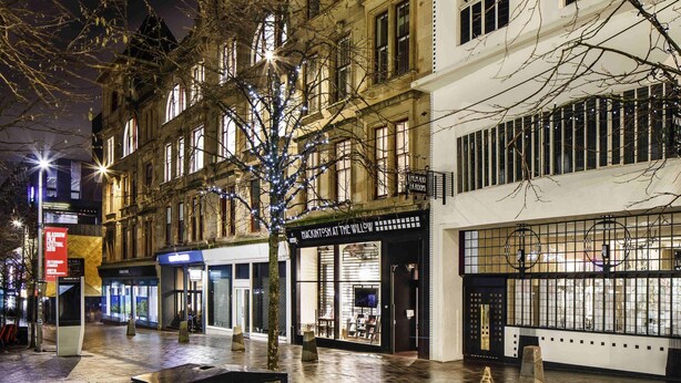 A nighttime urban street with buildings, a tree with lights, and storefronts. - Ibis Glasgow City Centre – Sauchiehall St (Glasgow)