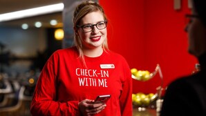 A person wearing a red shirt with the text "CHECK-IN WITH ME" holding a smartphone. - Ibis Glasgow City Centre – Sauchiehall St (Glasgow)