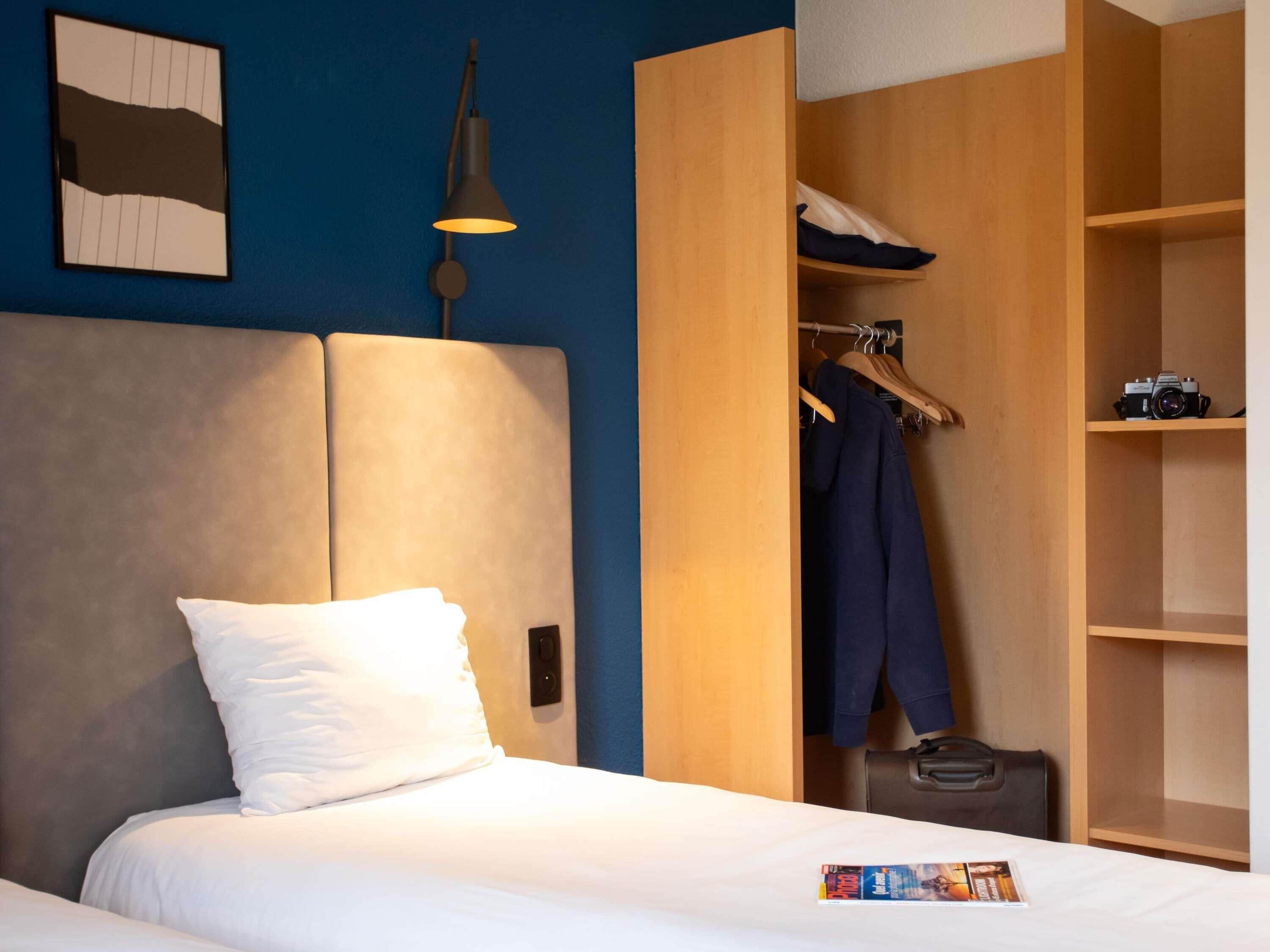 A hotel room with a bed, a wardrobe, and a hanging light fixture.
