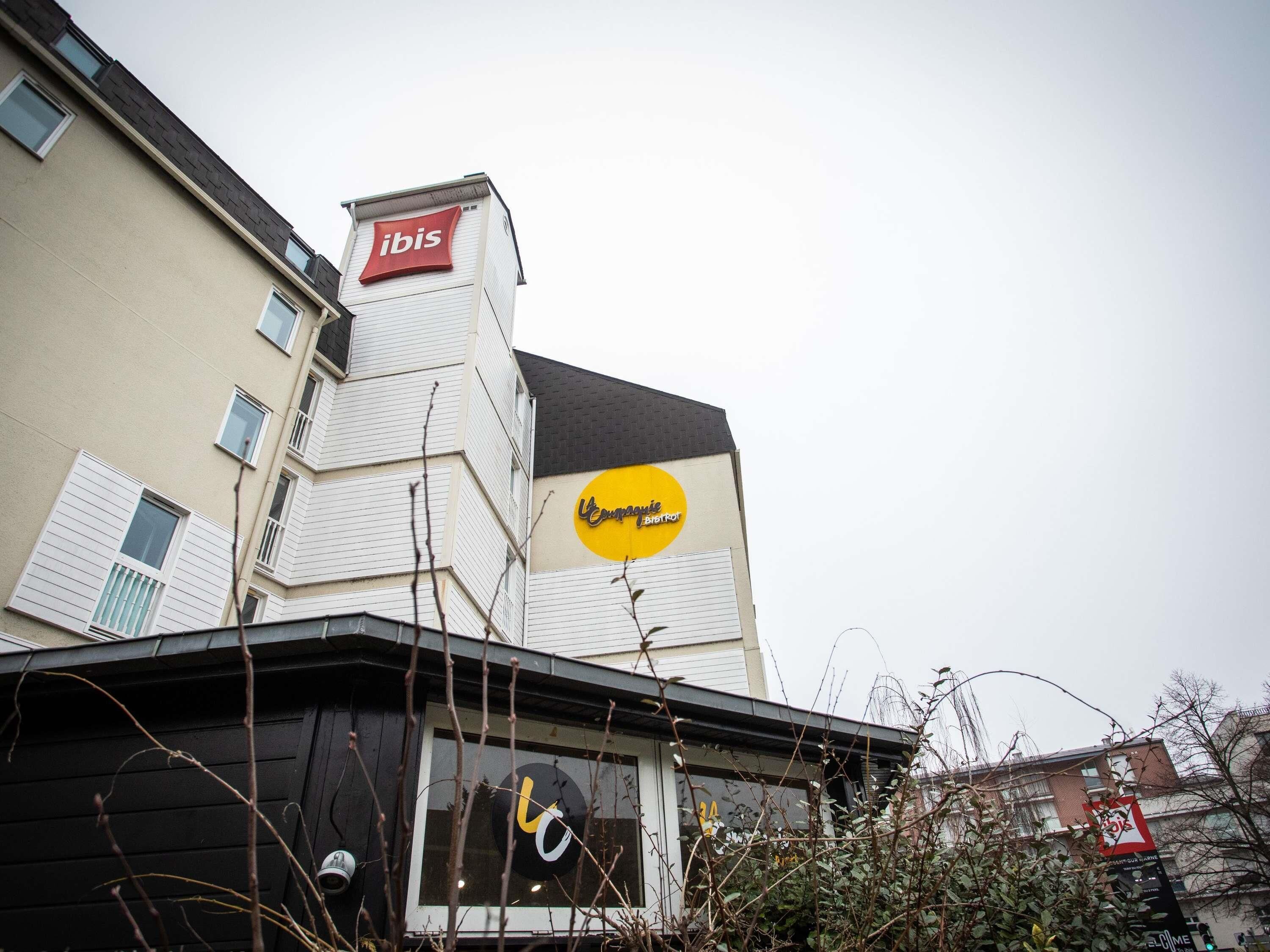 A building with a prominent 'ibis' sign, a large yellow circular logo, and a black awning with a white design.